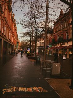 a city street with people walking on the sidewalk and buildings in the background at sunset