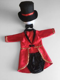 a red jacket and black pants with a top hat on the head is sitting next to a white wall