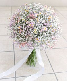 a bouquet of daisies and baby's breath tied to a white ribbon on a tiled floor