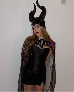 a woman in a costume with horns on her head is standing next to a wall