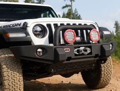 the front end of a white jeep driving down a dirt road