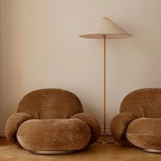 two brown chairs sitting next to each other in front of a lamp on a wooden floor