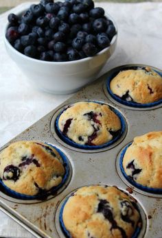 blueberry muffins sitting in a pan next to a bowl of berries