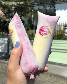 someone is holding two ice cream cones in their hand, one pink and the other white