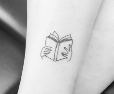 a woman's leg with a book tattoo on her left thigh and hands holding an open book