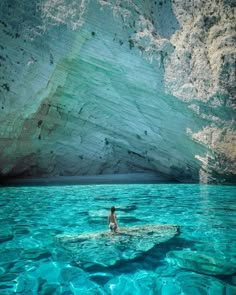 a person is swimming in the water near a large rock formation and cliffs that look like they have been carved out of stone