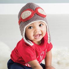 a small child wearing a crocheted hat and smiling at the camera while sitting on a bed