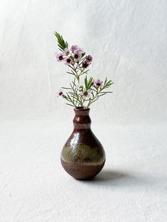 a brown vase with flowers in it on a white surface and the background is plain