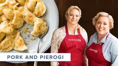 two women in red aprons standing next to a plate of chicken and pierogi