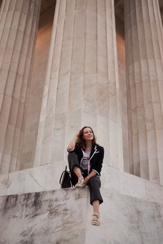 a woman sitting on the side of a tall building next to columns with her hand in her hair