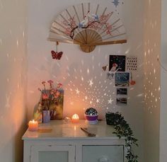 a white cabinet with candles and pictures on the wall behind it, in front of a fan