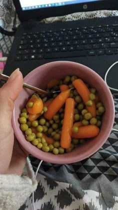 a person is holding a spoon in a bowl with peas and carrots on it