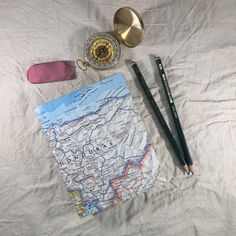 a map, compass and two pens on a bed