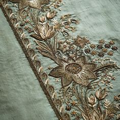 an embroidered piece with flowers and leaves in gold on a green background, close up