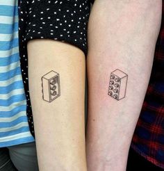 two people with matching tattoos on their arms, one has a dice and the other has a box