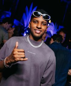 a man wearing sunglasses and giving the thumbs up sign at a party with other people in the background