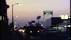 cars driving down the street at dusk in front of a banker bros sign and traffic lights