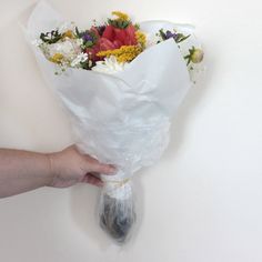 a person holding a bouquet of flowers on a white wall with their hand in it