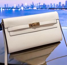 a white purse sitting on top of a table next to the ocean with a city skyline in the background