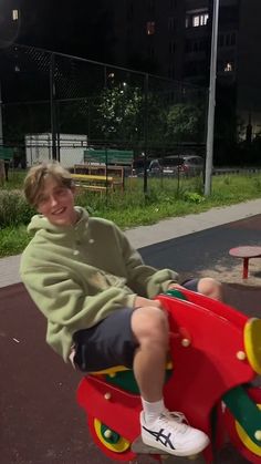 a young boy sitting on top of a red wooden toy car in a park at night