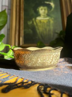 a gold bowl sitting on top of a table next to a green leafy plant