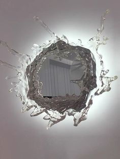 a mirror that is on the wall with water splashing from it's center