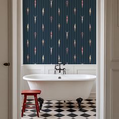 a bath tub sitting under a window next to a red stool