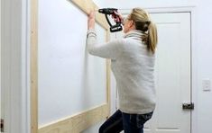 a woman is using a drill to attach the wall paneling in front of her