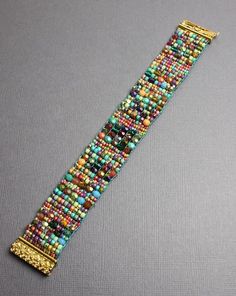 a beaded watch bracelet with gold clasps and colorful beads on a gray surface