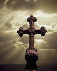 a cross on top of a pillar in the middle of the ocean under a cloudy sky