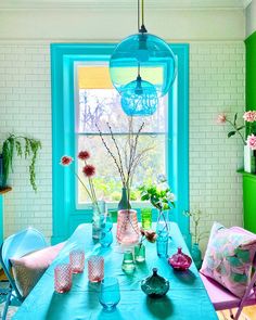 a dining room table with vases and flowers in front of a blue painted window