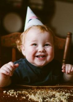 a little boy sitting at a table with a birthday hat on