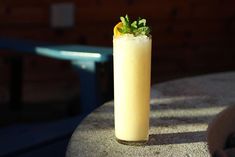 a tall glass filled with a drink sitting on top of a cement table next to a blue chair