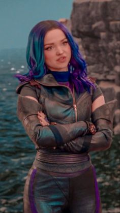 a woman with blue hair standing in front of the ocean wearing a black and purple outfit