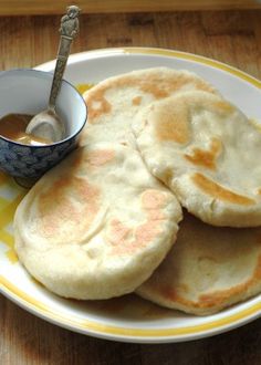 three flat breads on a yellow and white plate with a small bowl of sauce