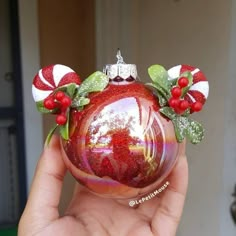 a hand holding a red ornament with holly and candy canes on it