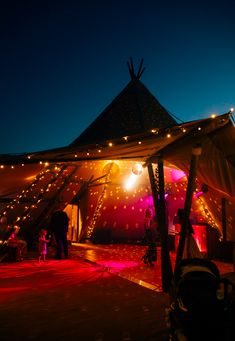 a tent that has lights on it and people in the background under it at night