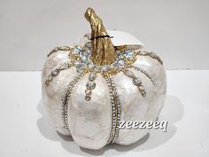 a white pumpkin decorated with gold and crystal jewels on it's side, sitting on a table