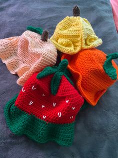 three crocheted strawberries are laying on a blue blanket and one is wearing a hat