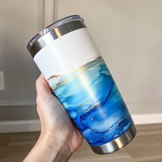 a hand holding a blue and white coffee cup with gold foiling on it's side