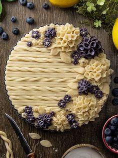 a pie with blueberries and flowers on it sitting next to some other food items