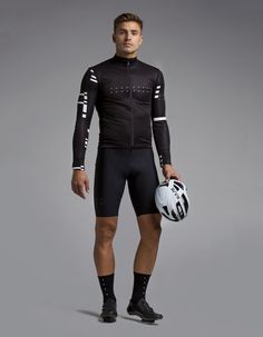 a man holding a soccer ball and helmet in front of a gray background wearing a black cycling suit