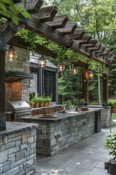 an outdoor kitchen with stone walls and grilling area, surrounded by greenery in the background