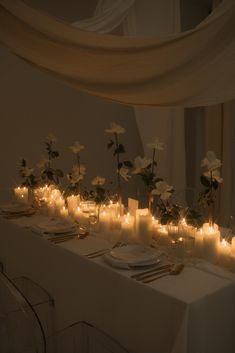 a long table is set with candles and flowers in vases, plates and silverware