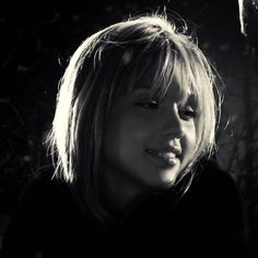 a black and white photo of a woman with blonde hair smiling at someone in the background