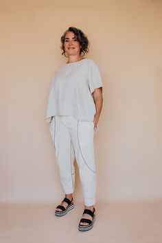 a woman standing in front of a wall wearing white pants and a t - shirt