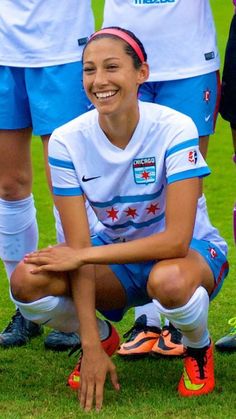 a woman sitting on the ground in front of soccer players wearing blue and white uniforms