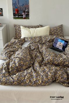 an open laptop computer sitting on top of a bed covered in floral sheets and pillows