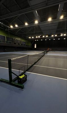 an empty tennis court with lights on and a racket in the middle of it