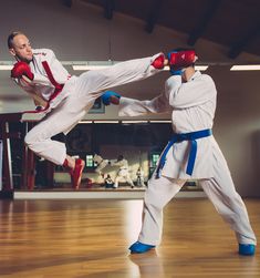 two men in white and red karate outfits kick punches at each other on a wooden floor